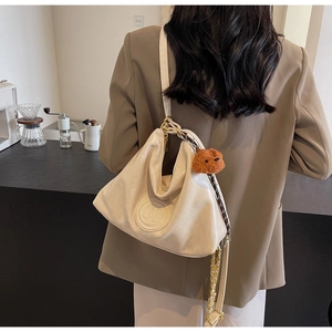 Detail of off-white faux leather tote bag with embossed M logo and plush bear charm