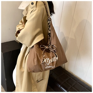 Detail einer braunen Tragetasche mit Leoparden-Schleife und Aufdruck auf einem Trenchcoat