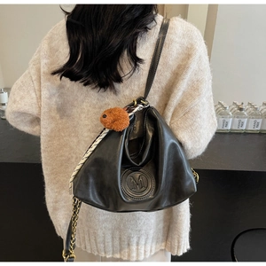 Detail of black leather shoulder bag with embossed M logo, plush charm and silk scarf wrap