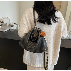 Detail of black leather shoulder bag with embossed M logo and brown teddy bear charm