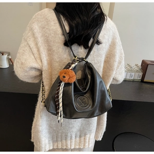 Black leather backpack with embossed M logo, bear charm, and chain strap on female model
