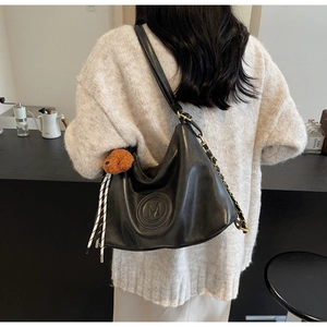 Detail of black leather hobo bag with embossed M logo and brown plush bear charm