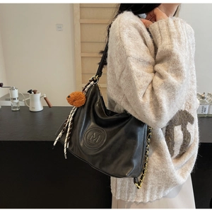 Detail of black leather tote bag featuring M embossing and plush bear charm detail