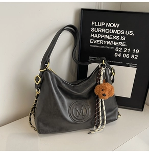 Detail of black leather shoulder bag with embossed M logo and brown teddy bear keychain