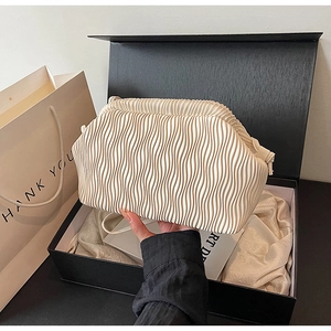 Nahaufnahme der beigen Plissee-Tasche mit Wellentextur und Lederriemen in einer Geschenkbox