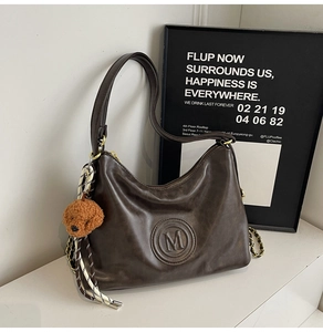 Detail of vintage dark brown faux leather tote with embossed logo and teddy bear charm
