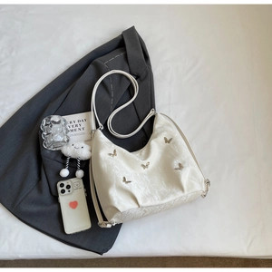 Detail of white wrinkled shoulder bag with five silver butterfly charms on a suit background