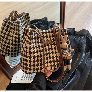 Detail of checkered woven tote bag with brown leather strap and rabbit charm