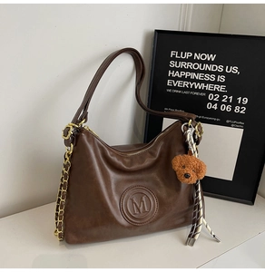 Close-up of vintage brown PU leather bag with embossed M logo and plush bear charm decoration