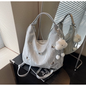 Detail of silver hobo bag with butterfly charms and fluffy cloud keychain in chic setting