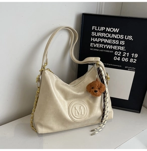 Detail of ivory faux leather shoulder bag with embossed M logo and plush bear charm