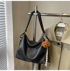 Detail view of black faux leather tote featuring M-embossed logo and cute puppy keychain