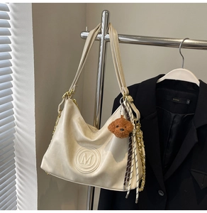 Detail of off-white faux leather tote with embossed M logo and brown plush dog charm