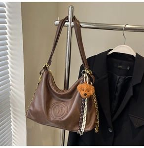 Detail of vintage brown leather tote with M logo, gold chain, and cute dog charm accessory