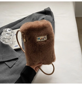 Détail du sac bandoulière en peluche marron avec logo sur fond de veste grise