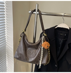 Detail of dark brown faux leather tote bag with M logo embossing and cute dog keychain