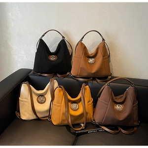 Detail view of large tote bag with metal M-logo in black brown beige and yellow