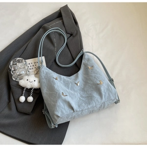 Close-up of light blue hobo bag with butterfly metal accents and plush cloud charm