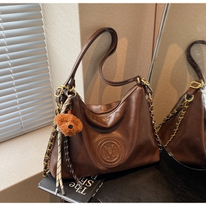 Detail of dark brown vintage faux leather tote with embossed M logo and plush puppy charm