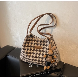 Macro detail of houndstooth tote bag with leather straps and cute bunny charm on a book