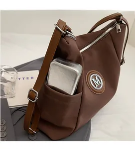 Detailed macro view of brown nylon tote bag with leather strap and metal M logo embellishment