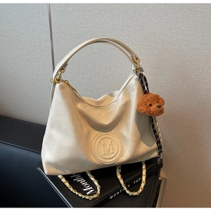 Detail of cream hobo bag with embossed M logo, gold chain strap and teddy bear charm