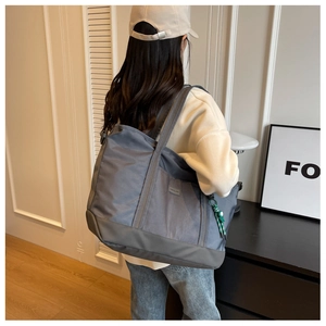 Rear view of a large grey nylon tote bag with decorative woven charm on a model