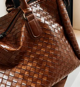 Detail of premium dark brown woven leather texture and sturdy metal zipper on travel bag