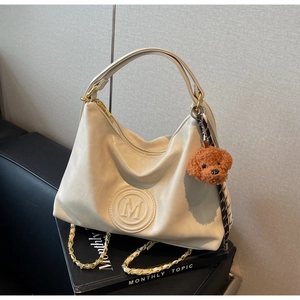 Detail of off-white PU leather tote bag with embossed M logo and cute teddy bear charm