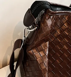 Detail of woven leather texture and silver metal hook on a large brown travel tote bag