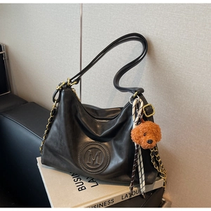 Detail of black faux leather tote with embossed M logo and brown plush puppy keychain