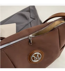Close-up of brown suede bag featuring silver M logo and smooth metal zipper detail