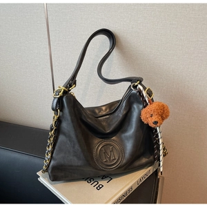 Detail of black matte leather tote bag with M embossing, gold chain, and teddy charm