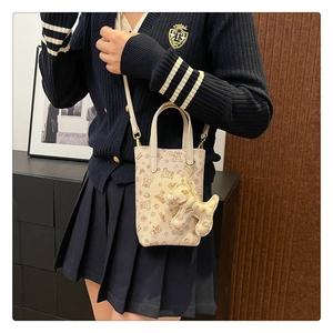Détail du petit sac bandoulière crème avec motif ours et breloque chien sur modèle