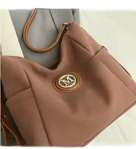 Close-up of silver metal M logo on brown matte leather tote bag with fine stitching