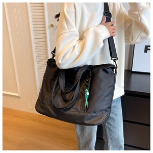 Close-up of black large-capacity travel bag with adjustable strap and green woven pendant