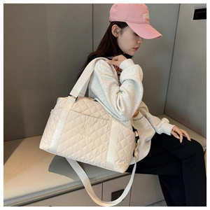 Large beige quilted travel bag with logo detail shown on a model in a casual setting
