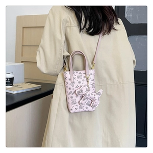 Mini sac bandoulière rose imprimé ours avec charm chien assorti posé sur une table en bois