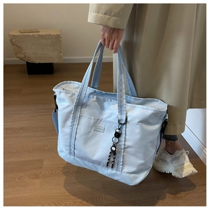Close-up of light blue travel bag with metal logo, reinforced handles and shoulder strap