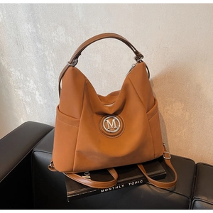 Detail view of brown faux leather tote with silver M logo and side pockets