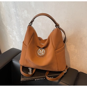 Detail of caramel tote bag showing M metal buckle, side pocket, and adjustable strap