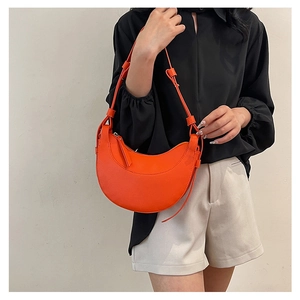 Dettaglio della borsa a mezzaluna arancione con trama litchi indossata a tracolla dalla modella