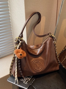 Vintage brown faux leather backpack with M-logo and gold chain strap in a warm setting