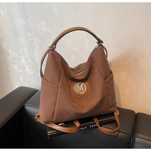 Detail view of the brown leather tote bag with a metal M logo on a black sofa