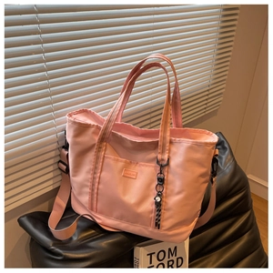 Pink nylon tote bag with front pocket and shoulder strap on leather seat near window