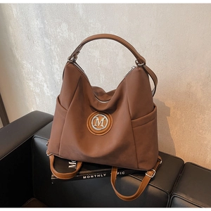 Close-up of caramel tote backpack with metal M logo on a leather seat with magazines