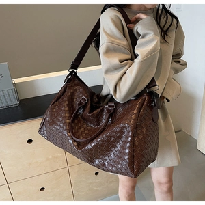 Detail of dark brown woven leather travel tote bag showing texture and shoulder strap
