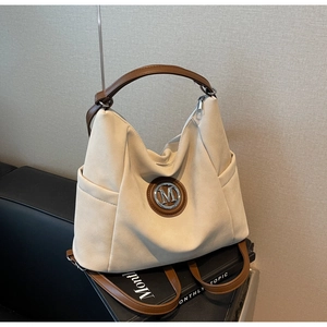 Detail of beige tote bag with matte texture, brown leather handles, and metal M logo