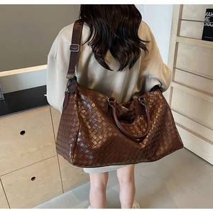 Detail of dark brown woven leather travel tote bag with double handles and wide strap