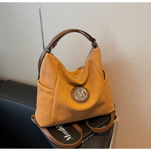 Detail of yellow tote bag with metallic M logo and adjustable brown leather straps